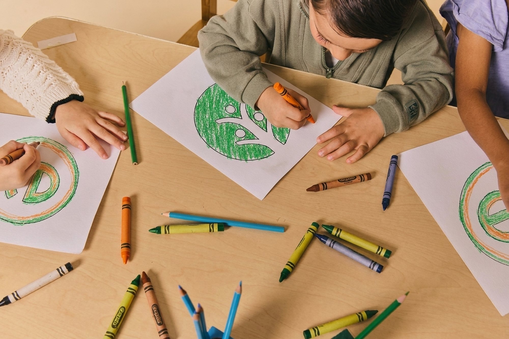 Children drawing a green leaf at a wooden table