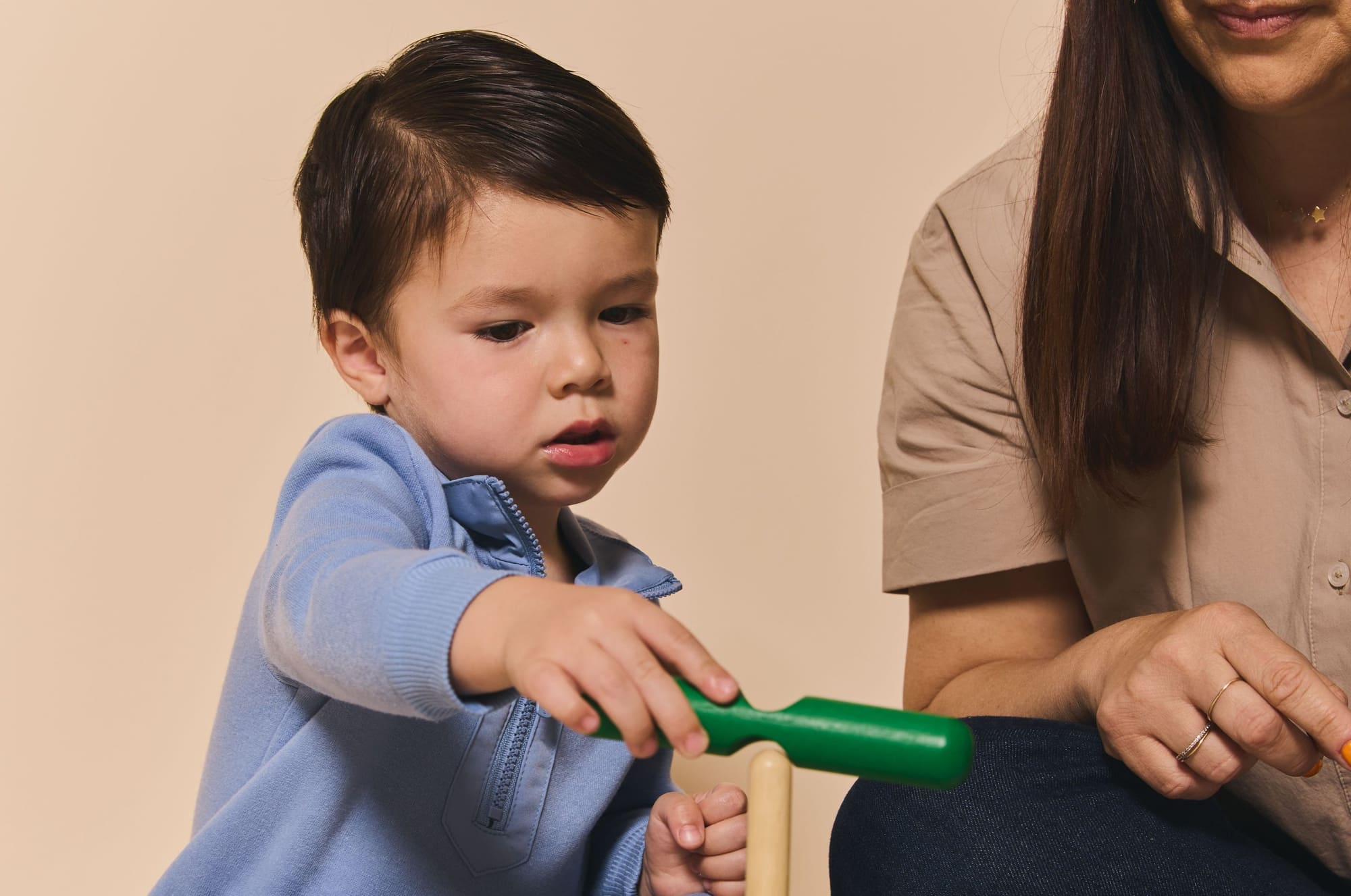 A toddler exploring a toy with his teacher beside him in our Little Nest room
